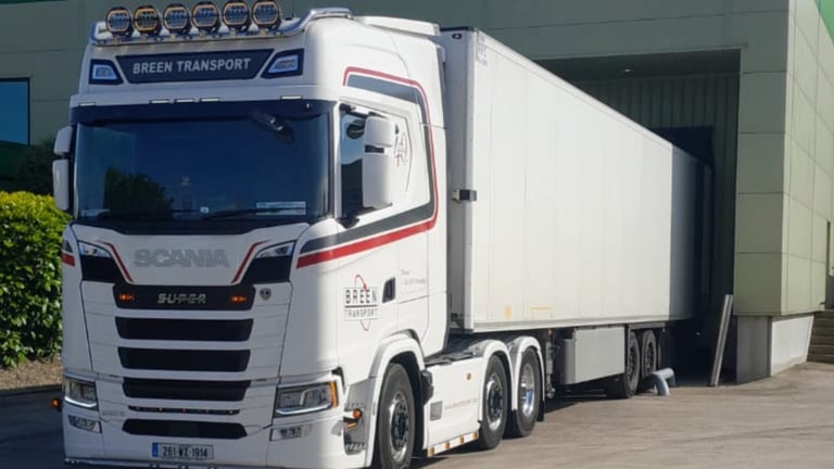 White Scania articulated truck with refrigerated trailer parked at a loading facility