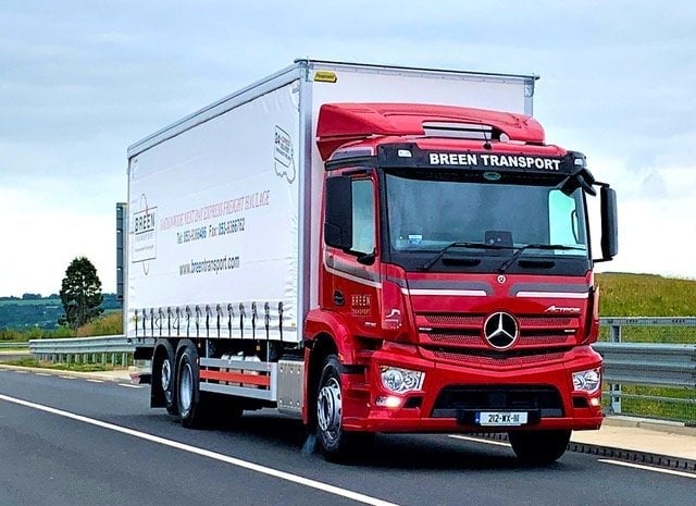 Red Mercedes delivery truck with white refrigerated box trailer driving on highway